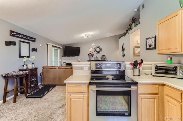 kitchen featuring stainless steel range with electric cooktop, lofted ceiling, kitchen peninsula, light carpet, and light brown cabinetry