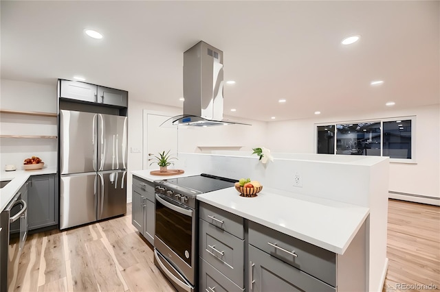 kitchen featuring island exhaust hood, appliances with stainless steel finishes, gray cabinetry, baseboard heating, and light hardwood / wood-style floors