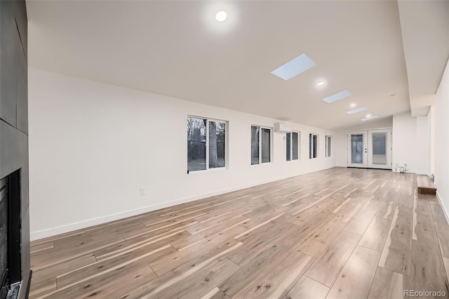 unfurnished living room featuring vaulted ceiling with skylight, light hardwood / wood-style floors, and french doors