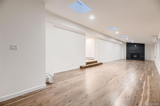 unfurnished living room featuring a fireplace, light hardwood / wood-style flooring, a skylight, and a baseboard heating unit