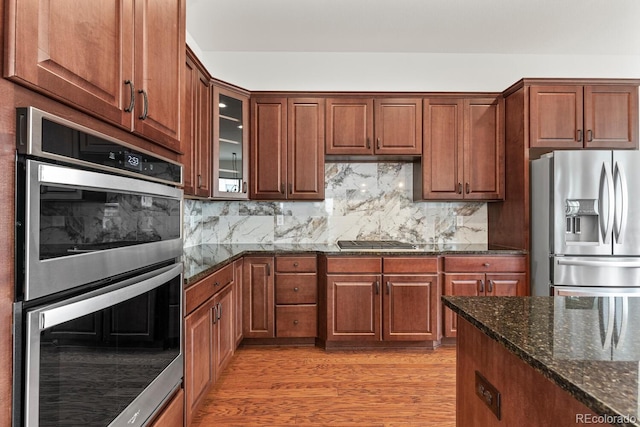 kitchen with stainless steel appliances, dark stone countertops, backsplash, and light hardwood / wood-style flooring