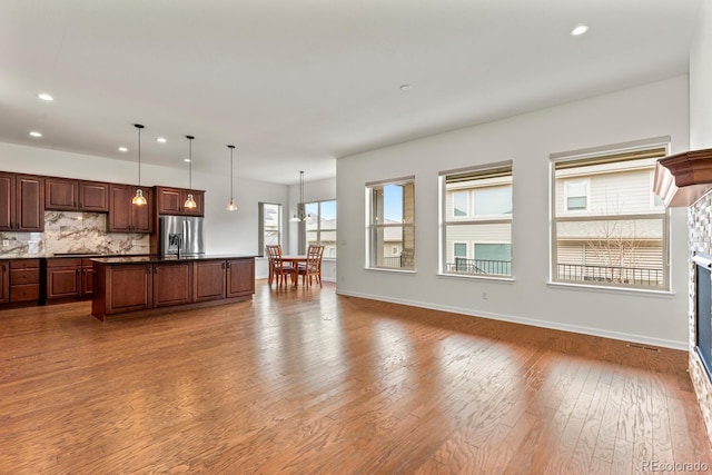 kitchen with hardwood / wood-style flooring, stainless steel refrigerator with ice dispenser, a center island with sink, and decorative light fixtures