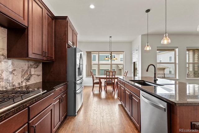 kitchen featuring sink, hanging light fixtures, dark stone counters, stainless steel appliances, and a kitchen island with sink