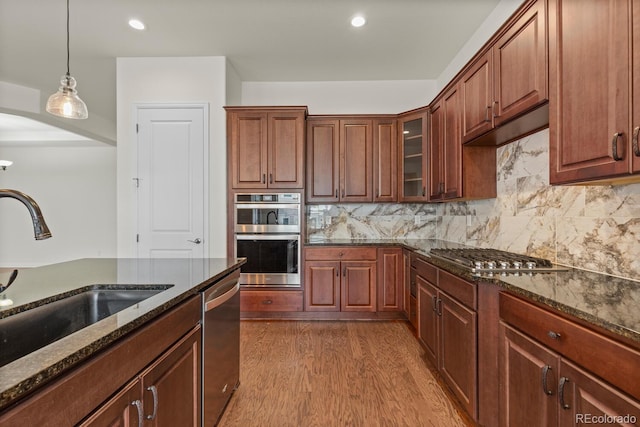 kitchen with appliances with stainless steel finishes, hardwood / wood-style floors, sink, dark stone counters, and hanging light fixtures