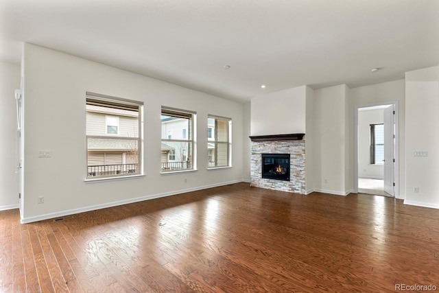 unfurnished living room with a stone fireplace and dark wood-type flooring