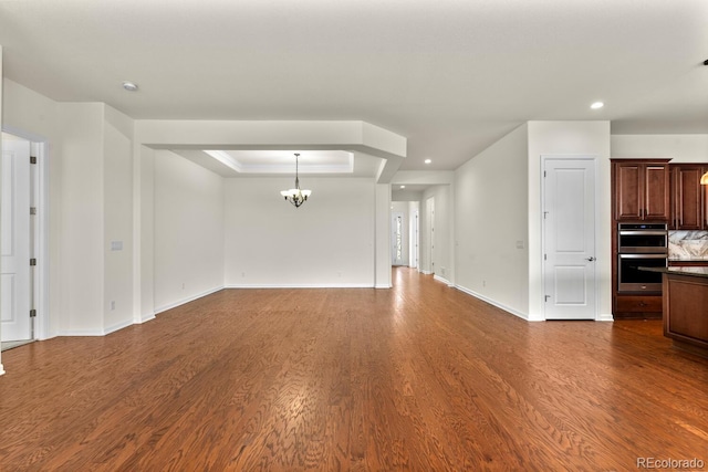 unfurnished living room featuring an inviting chandelier, hardwood / wood-style floors, and a raised ceiling