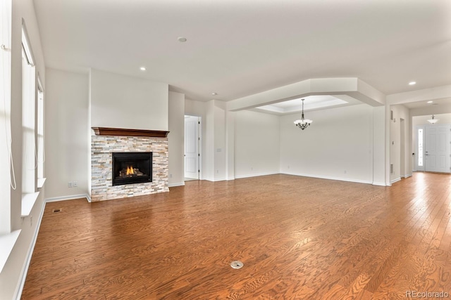 unfurnished living room with hardwood / wood-style flooring, a raised ceiling, an inviting chandelier, and a fireplace