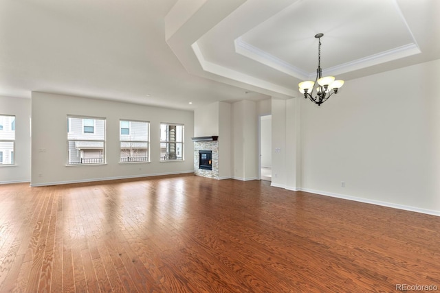 unfurnished living room featuring an inviting chandelier, a tray ceiling, a fireplace, and wood-type flooring