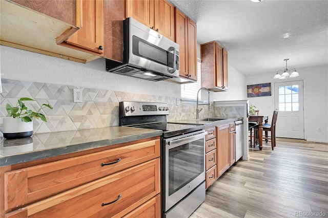 2791 Quarterland St, Strasburg, CO 80136 - kitchen featuring appliances with stainless steel finishes, a sink, a chandelier, light wood finished floors, and decorative backsplash