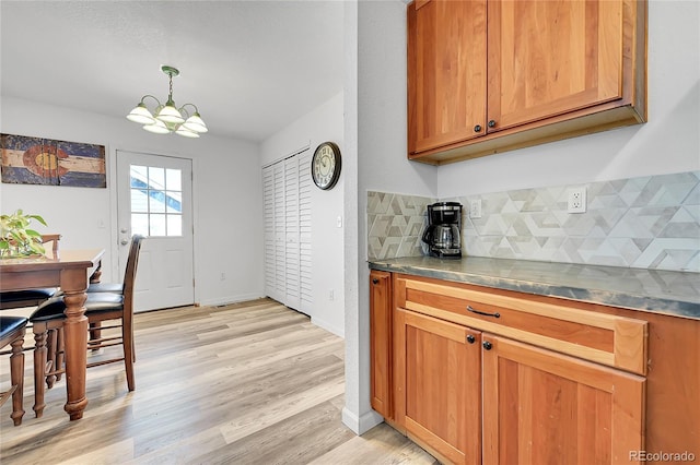 2791 Quarterland St, Strasburg, CO 80136 - kitchen with decorative backsplash, brown cabinetry, light wood-type flooring, a chandelier, and pendant lighting