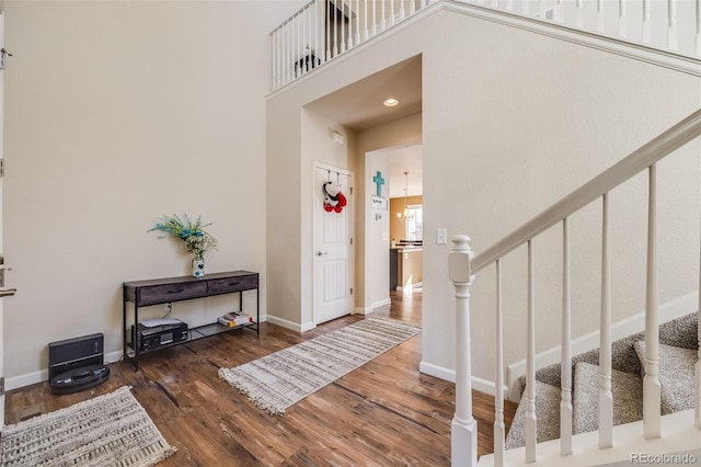 foyer entrance featuring a towering ceiling, stairs, baseboards, and wood finished floors