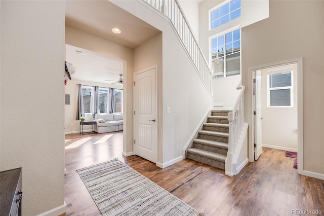 staircase with a high ceiling, recessed lighting, wood finished floors, and baseboards