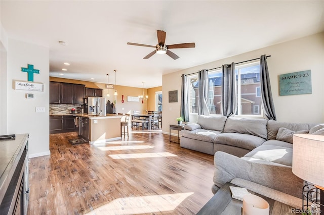 living room featuring ceiling fan with notable chandelier, recessed lighting, wood finished floors, and baseboards