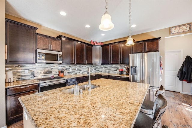 kitchen with stainless steel appliances, a sink, light wood-style floors, dark brown cabinets, and decorative backsplash