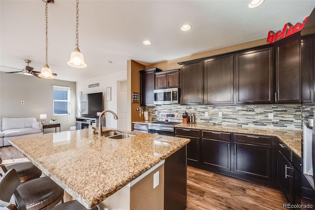 kitchen with tasteful backsplash, appliances with stainless steel finishes, open floor plan, light stone countertops, and a sink