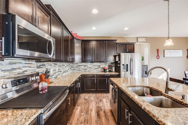 kitchen with tasteful backsplash, appliances with stainless steel finishes, hanging light fixtures, light stone countertops, and a sink