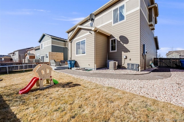 back of property featuring a lawn, a playground, fence, and cooling unit