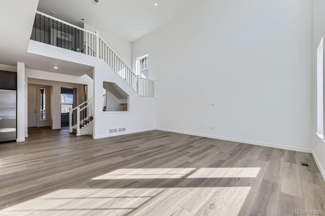 unfurnished living room featuring stairs, a healthy amount of sunlight, visible vents, and light wood-style floors