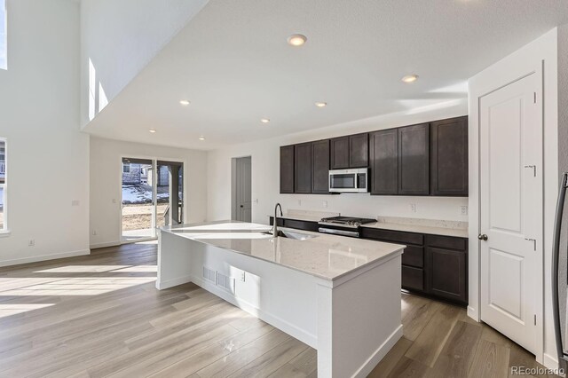 kitchen featuring recessed lighting, appliances with stainless steel finishes, light wood-style floors, a sink, and dark brown cabinetry