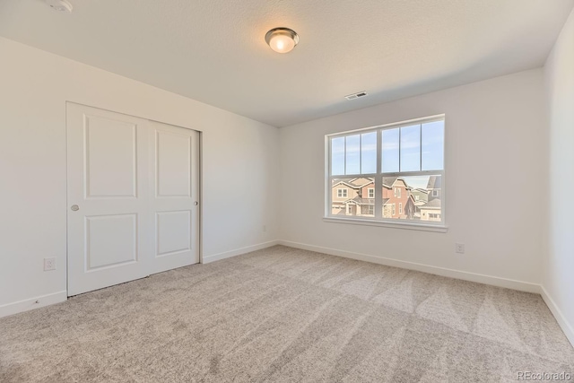 unfurnished bedroom with a textured ceiling, carpet, visible vents, and baseboards