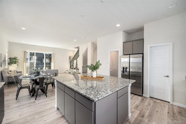 kitchen with light wood-type flooring, gray cabinets, a kitchen island, open floor plan, and stainless steel fridge