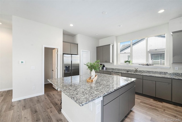 kitchen with gray cabinetry, recessed lighting, appliances with stainless steel finishes, light wood finished floors, and light stone countertops