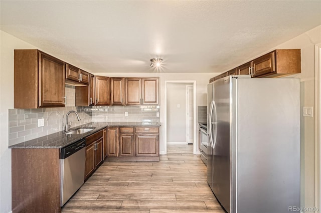 2201 S Holly St Unit 1, Denver, CO 80222 - kitchen featuring appliances with stainless steel finishes, dark stone countertops, light wood-type flooring, tasteful backsplash, and brown cabinetry