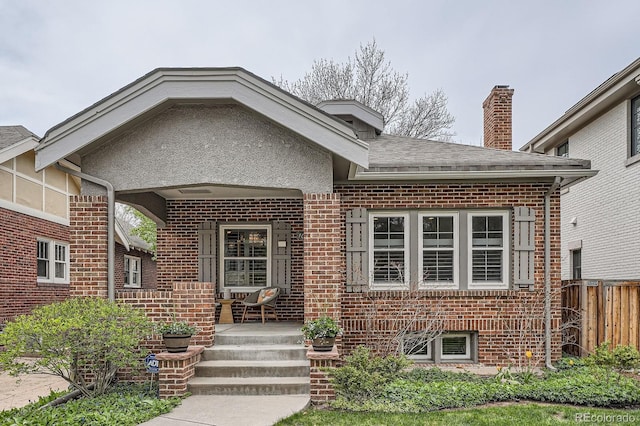 view of front of property with a porch, roof with shingles, fence, brick siding, and a chimney