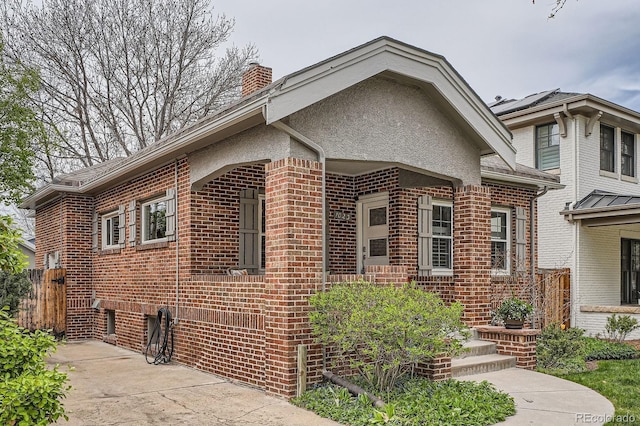 view of front of home with brick siding, a chimney, and fence