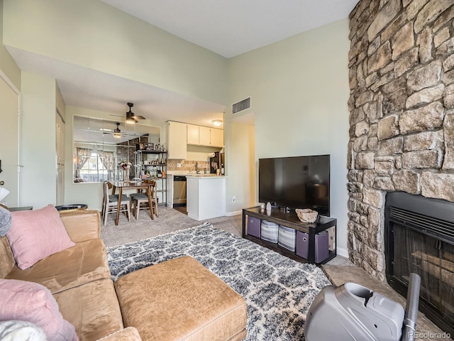 carpeted living room featuring ceiling fan and a stone fireplace