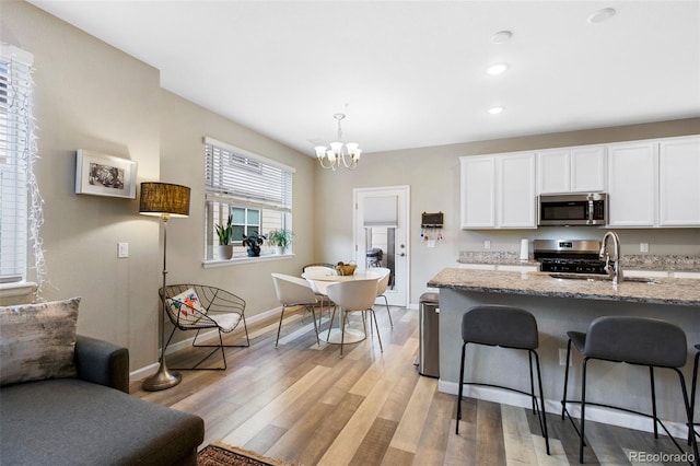 kitchen featuring a breakfast bar, a sink, stainless steel microwave, gas range oven, and baseboards