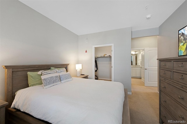 bedroom with light carpet, ensuite bathroom, baseboards, and a spacious closet