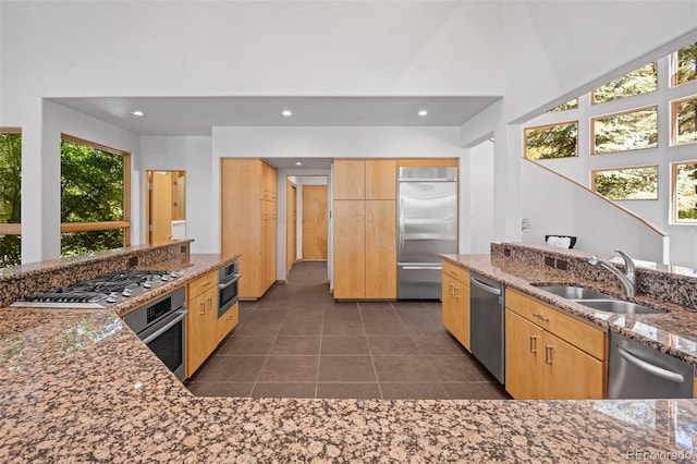 kitchen with stone countertops, sink, dark tile patterned flooring, stainless steel appliances, and light brown cabinets