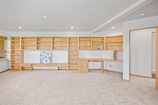 unfurnished living room featuring built in desk, light colored carpet, and beam ceiling