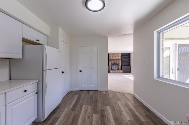 2120 S Ouray St, Aurora, CO 80013 - kitchen with freestanding refrigerator, white cabinetry, dark wood-type flooring, a brick fireplace, and light countertops