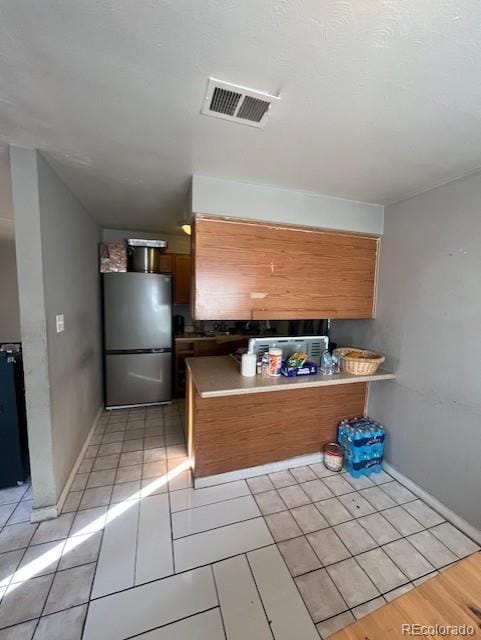 kitchen featuring light tile patterned floors, stainless steel refrigerator, and kitchen peninsula