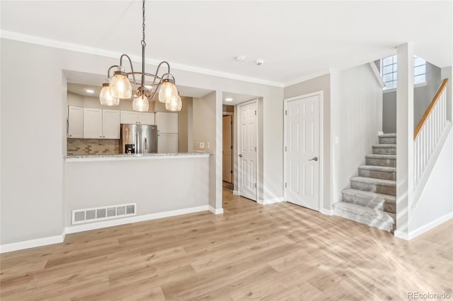 kitchen with white cabinetry, light stone counters, decorative light fixtures, light wood-type flooring, and stainless steel fridge