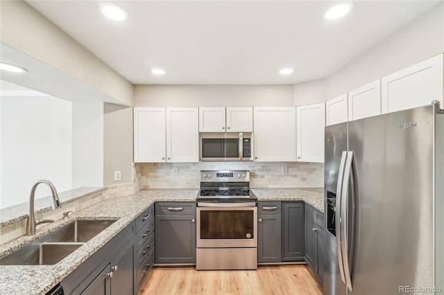 kitchen with sink, gray cabinetry, white cabinetry, stainless steel appliances, and light stone countertops