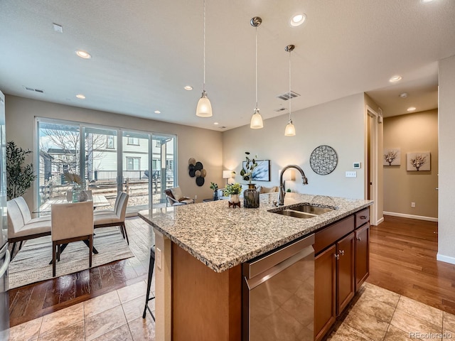 kitchen featuring a center island with sink, dishwasher, light stone counters, pendant lighting, and a sink