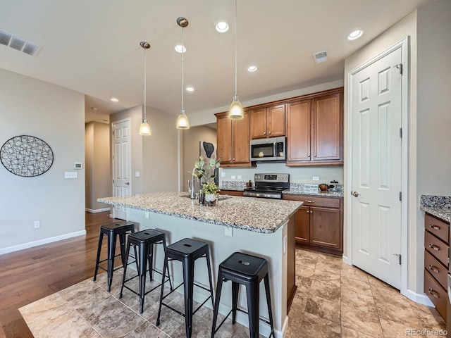 kitchen with a center island with sink, appliances with stainless steel finishes, a breakfast bar area, light stone countertops, and a sink