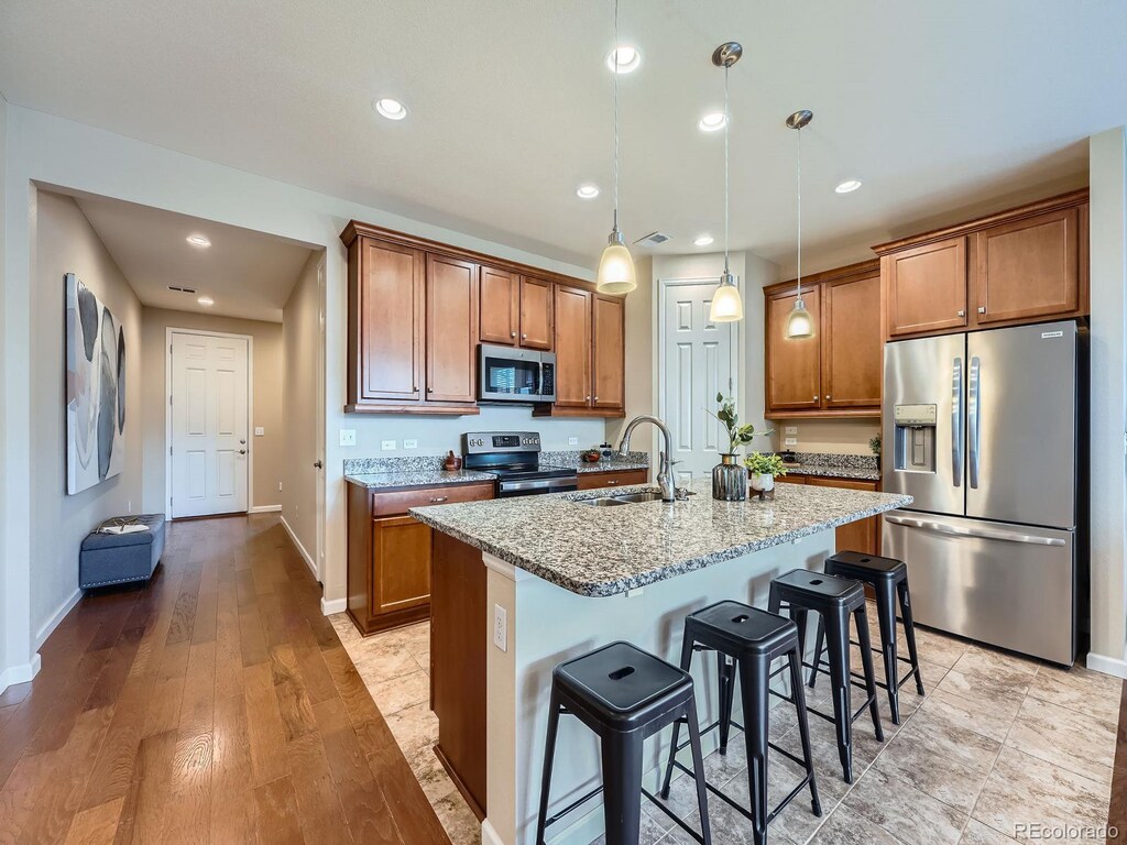 kitchen with a sink, light stone counters, brown cabinets, and appliances with stainless steel finishes