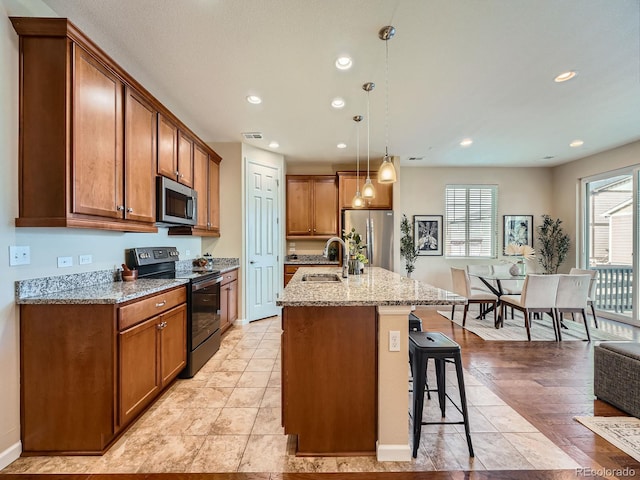 kitchen featuring brown cabinetry, light stone counters, a breakfast bar, stainless steel appliances, and a sink