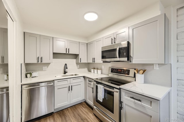 kitchen featuring sink, dark hardwood / wood-style flooring, stainless steel appliances, light stone counters, and decorative backsplash