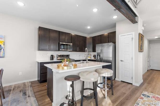 kitchen with a center island with sink, beam ceiling, light hardwood / wood-style flooring, dark brown cabinetry, and appliances with stainless steel finishes