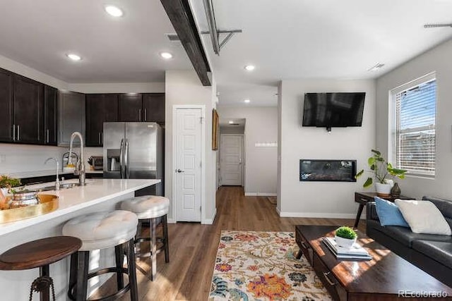 kitchen with a kitchen bar, dark brown cabinets, sink, dark hardwood / wood-style flooring, and stainless steel fridge