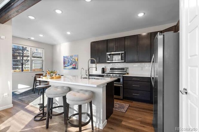 kitchen with a center island with sink, appliances with stainless steel finishes, a kitchen breakfast bar, wood-type flooring, and sink