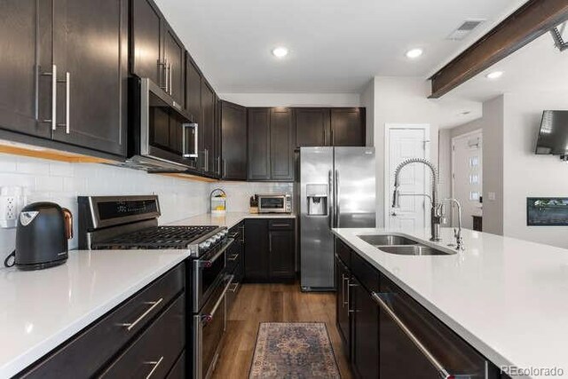 kitchen with stainless steel appliances, sink, dark brown cabinets, dark hardwood / wood-style floors, and beam ceiling