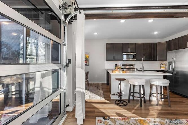 kitchen with a center island with sink, hardwood / wood-style flooring, dark brown cabinetry, a kitchen breakfast bar, and stainless steel appliances