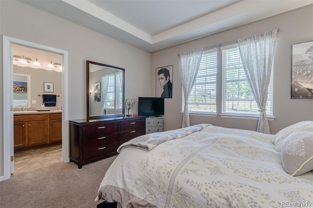 bedroom featuring ensuite bathroom, a tray ceiling, multiple windows, and light colored carpet