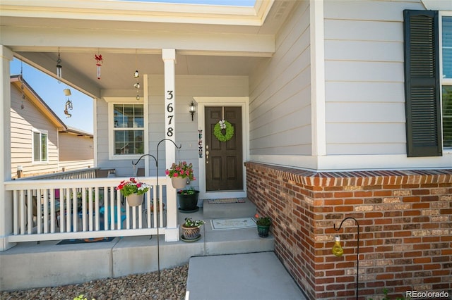 doorway to property featuring covered porch and brick siding